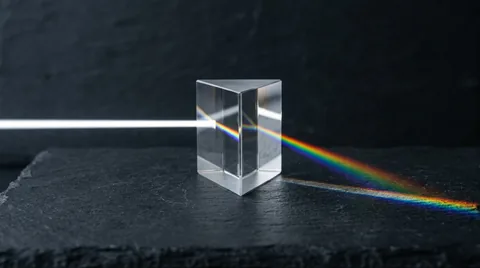 Minimalist glass prism on dark slate refracting a beam of white light into a crisp rainbow spectrum